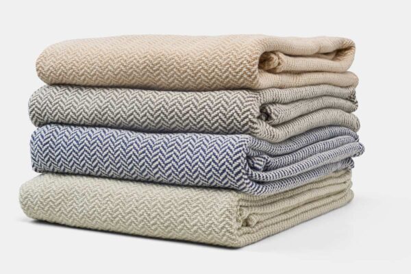 Various Organic Cotton Blankets stacked with Herringbone Weave in Various Colors Harvest, Grey, Blue, Green
