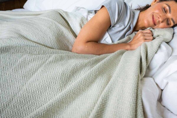 Woman in bed with an Organic Cotton Blanket with Herringbone Weave in Green